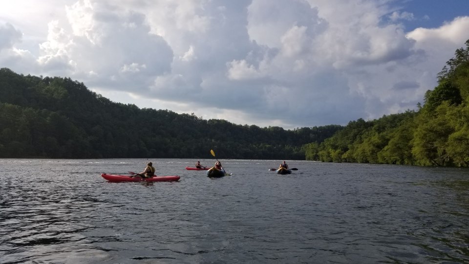 group of people far away paddling on a lake with mountains in the distance covered in trees