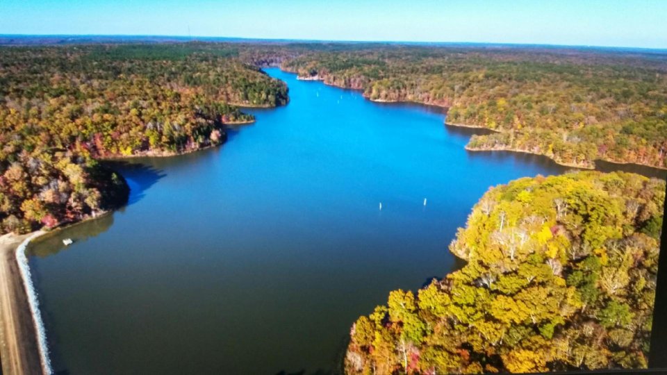 Aerial view of a vibrant blue lake surrounded by autumn-colored forests.