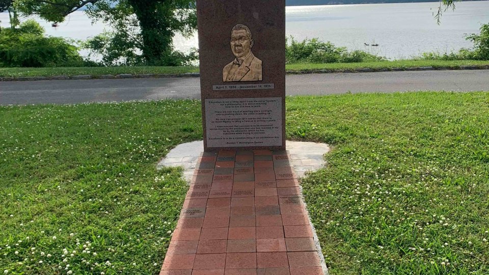 Brick pathway leading to a commemorative plaque by a lake.