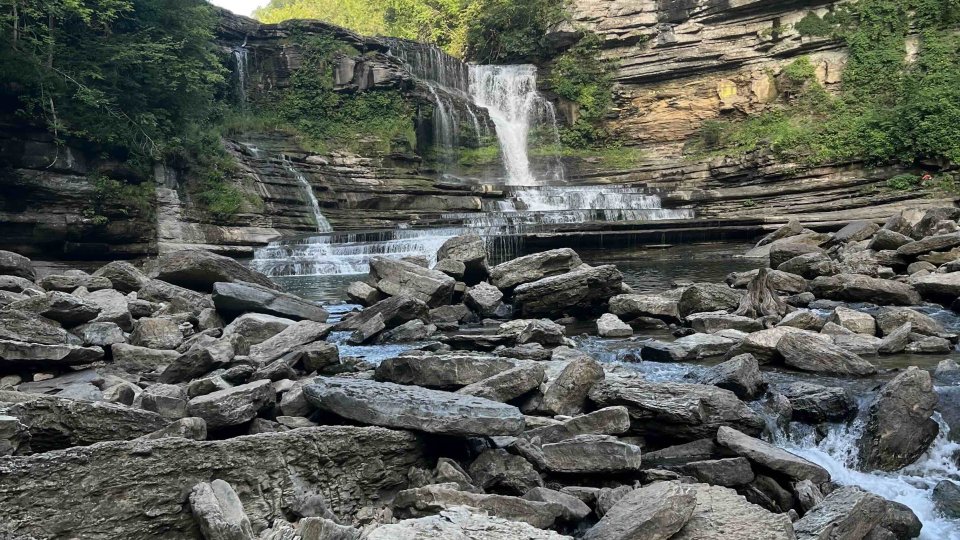 Cascading waterfall with surrounding cliffs and rocky riverbed.
