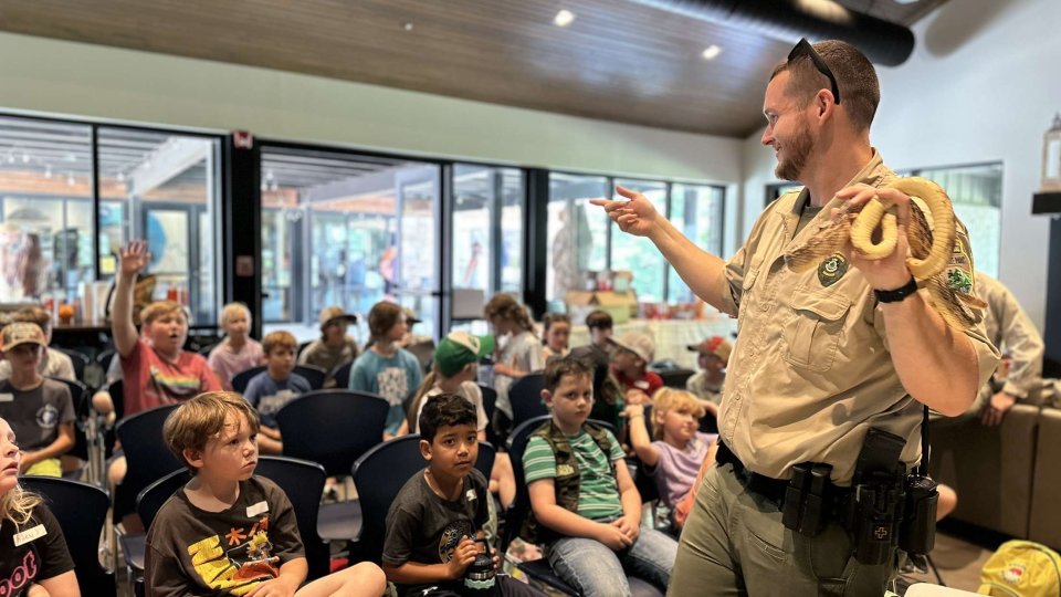 Ranger presenting a snake to a group of children in a classroom.