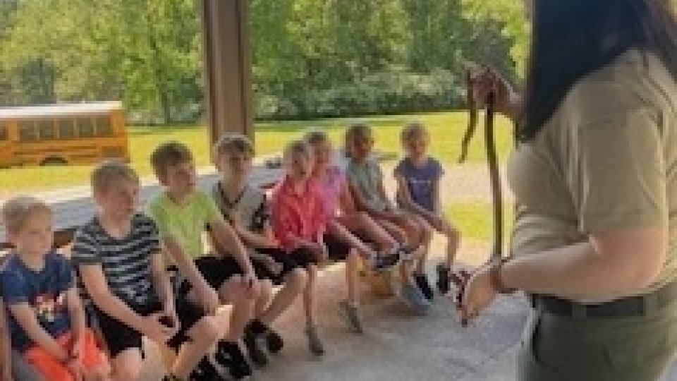 Park ranger showing a snake to a group of attentive children outdoors.