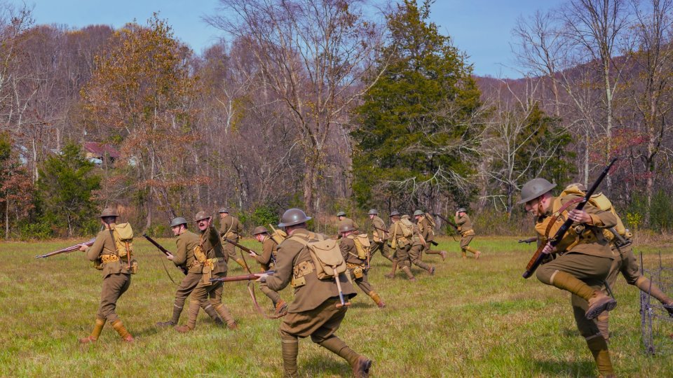 Historical reenactment of soldiers charging in a grassy field with rifles.