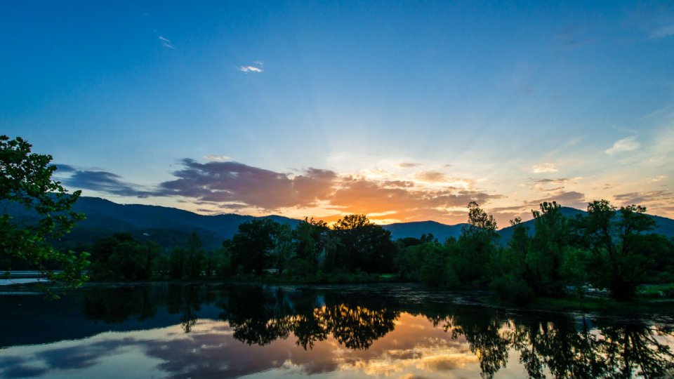 Sunset over a calm lake with reflected clouds and silhouetted mountains.
