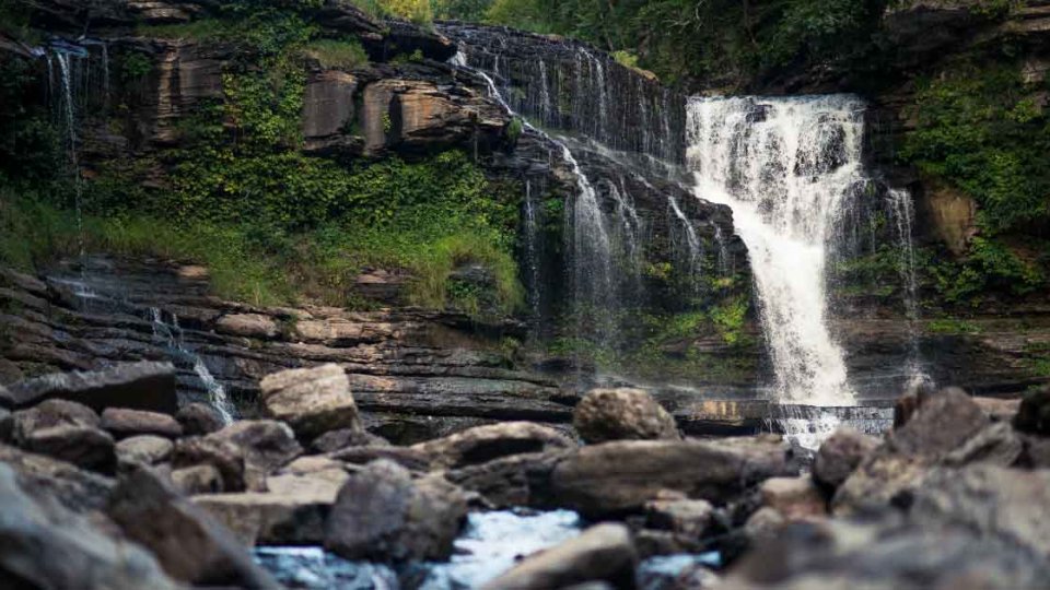 Waterfall cascading over rocky cliff into a boulder-strewn river.