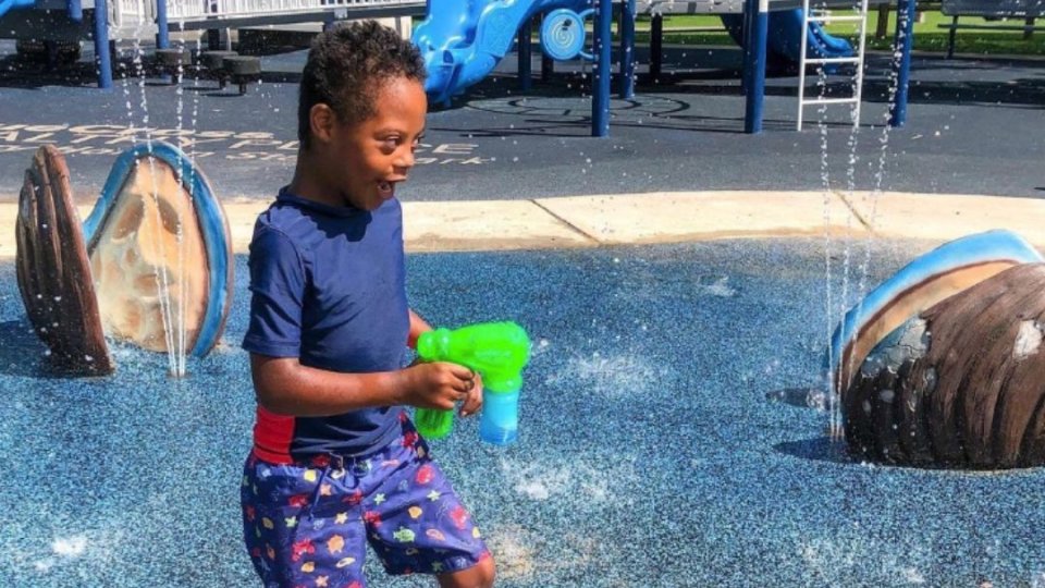 Young boy playing with water at a colorful splash pad playground.