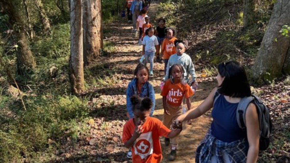 Group of children and adults hiking in a forest trail on a sunny day.