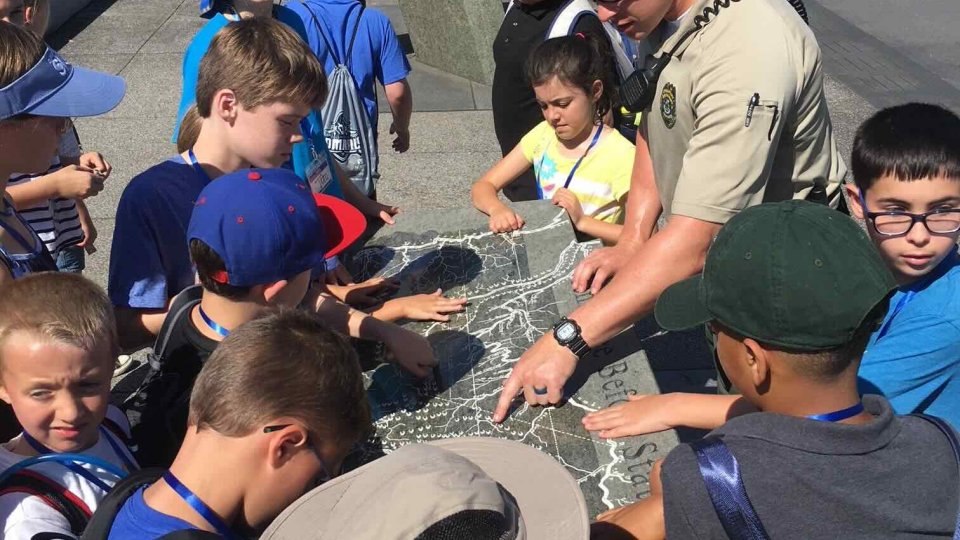 Park ranger showing a map to a group of attentive children outdoors.