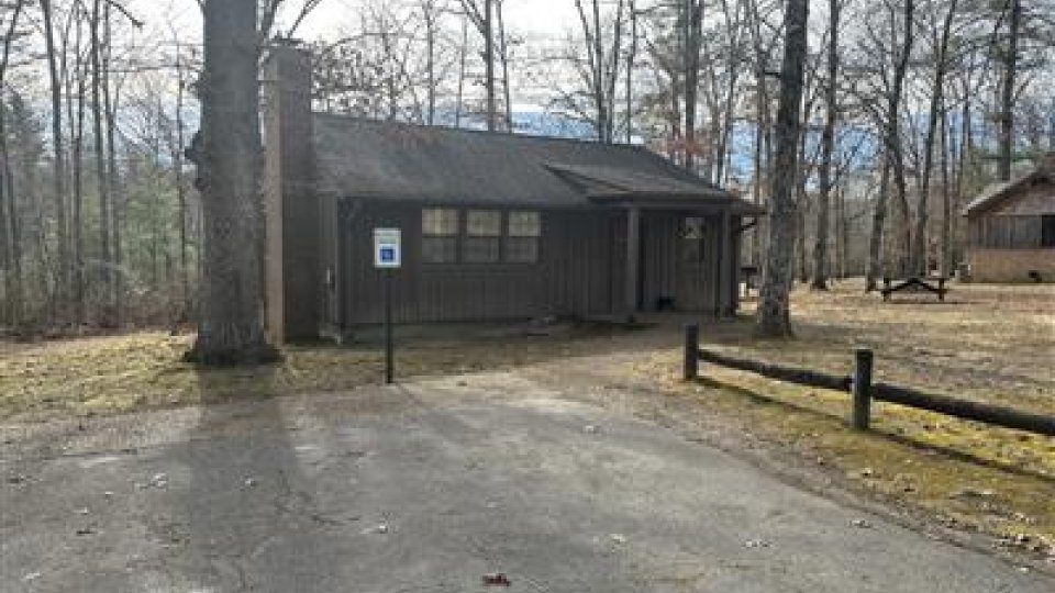 Brown cabin in a leafless forest with a paved driveway and a blue sign.