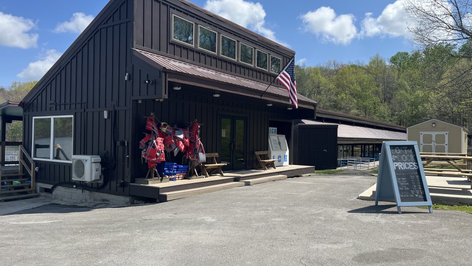 Dark wooden building with an American flag and people on the porch under clear skies.