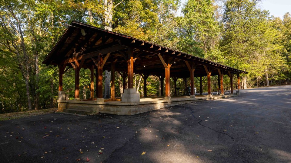 Wooden pavilion in a forest with a paved area on a sunny day.