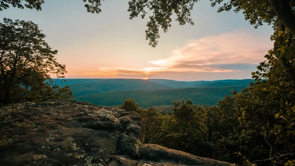 Sunset over a forested valley viewed from a rocky overlook.