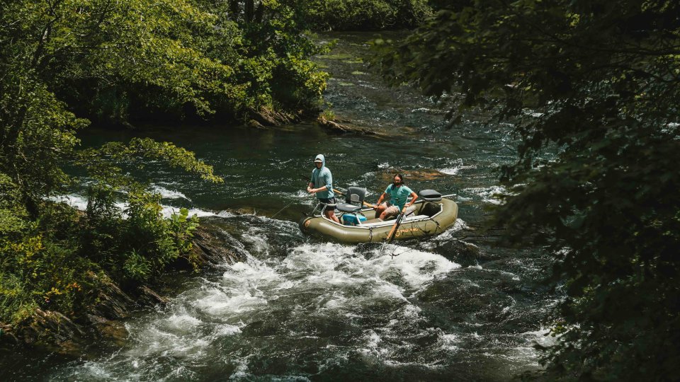 Two people rafting down a forested river.