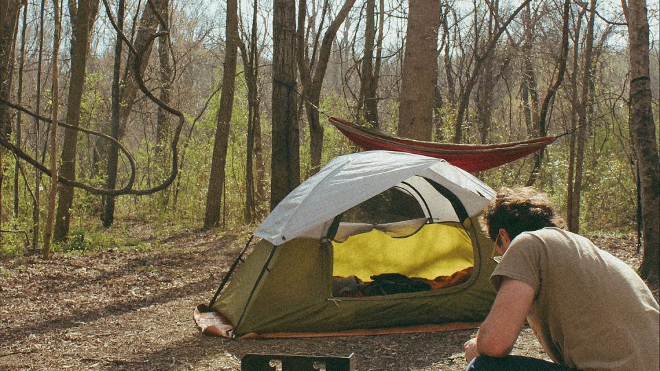 Person setting up a campfire near a tent in a forest.