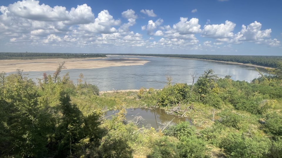 Lush green landscape with river, under a partly cloudy sky.