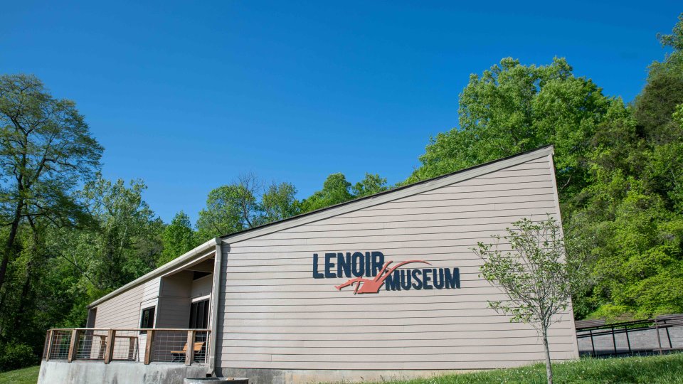 exterior of a white building that says "Lenoir Museum" surrounded by trees.