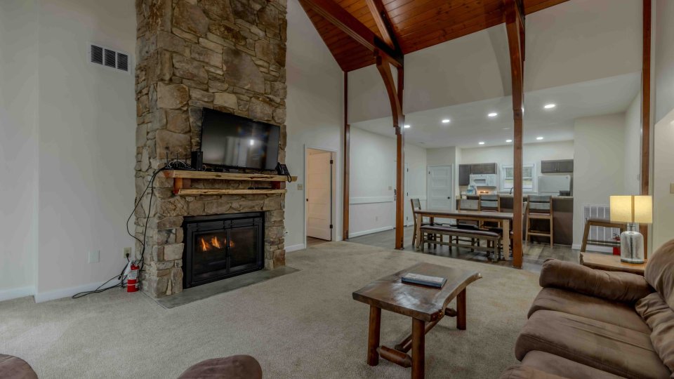 Cozy living room with stone fireplace, wooden beams, and plush furniture.