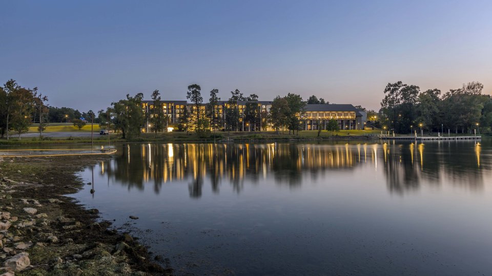 Twilight scene of a calm lake reflecting buildings and trees.
