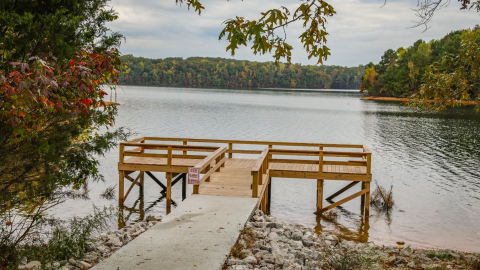 Wooden pier overlooking a tranquil lake surrounded by autumn trees.
