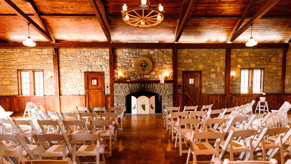 Rustic wedding venue with wooden beams and white chairs.
