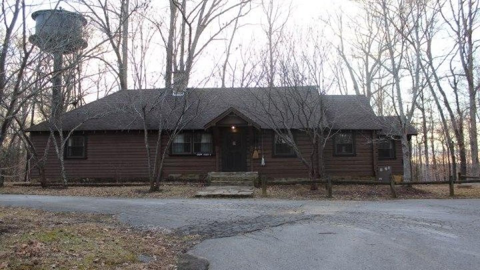 Brown cabin surrounded by leafless trees on an overcast day.