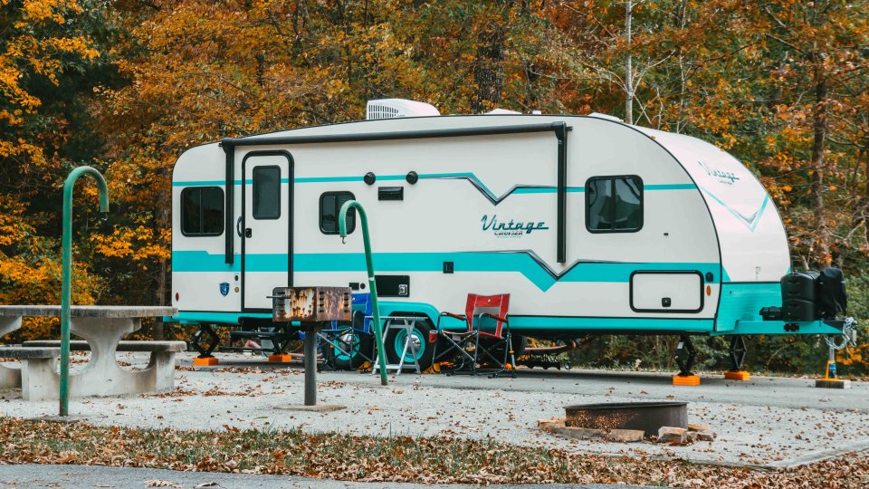 Modern teal and white camper parked in autumn forest campground.