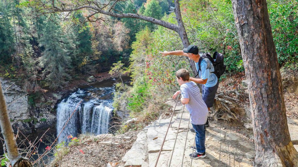 Two people hiking near a waterfall in a forest.