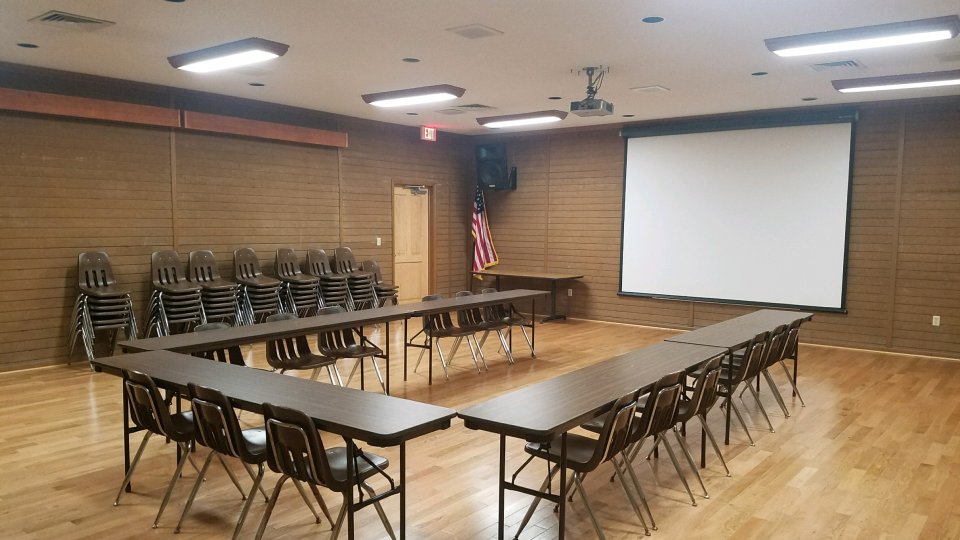 Empty meeting room with tables, chairs, and a projector screen.