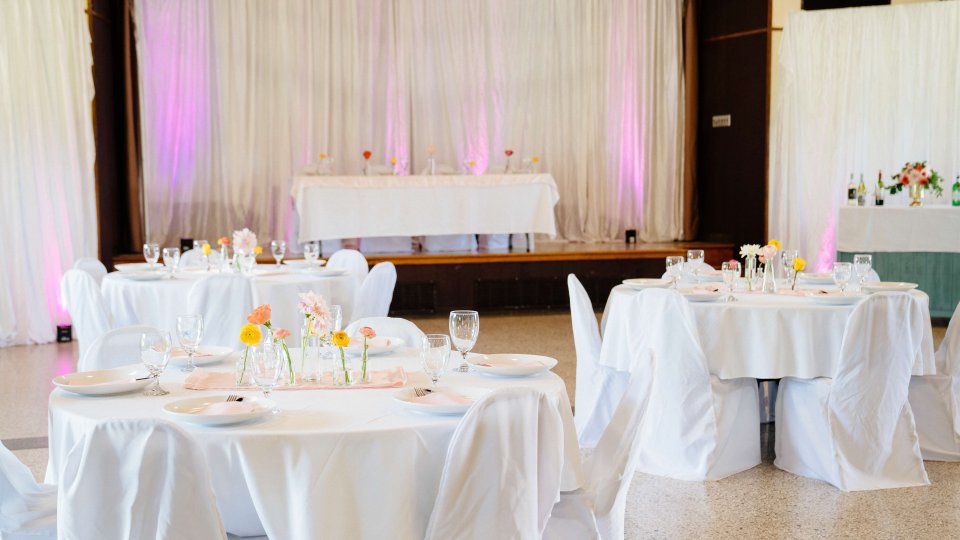 Elegant wedding reception hall decorated with white tablecloths and pink lighting.