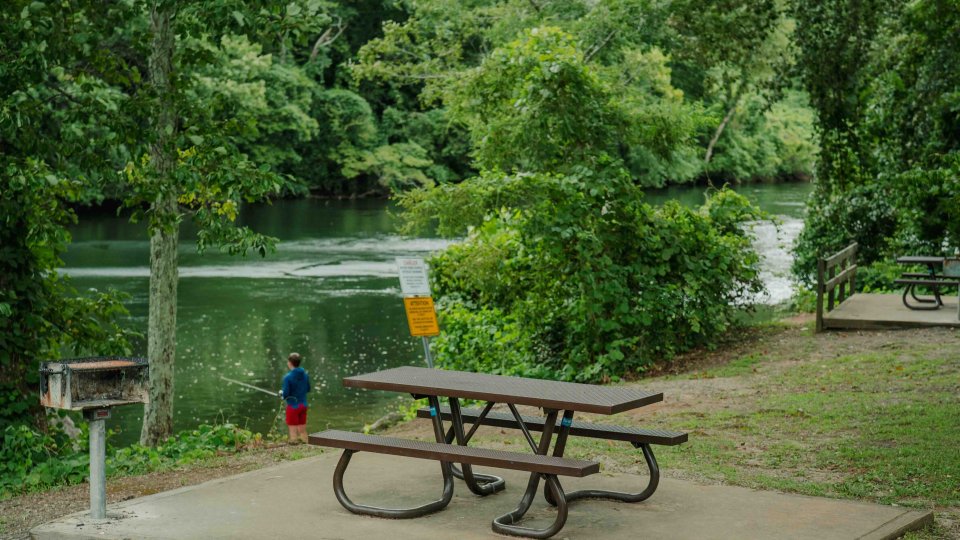 ADA accessible trail leading to a picnic table next to a grill and a river.