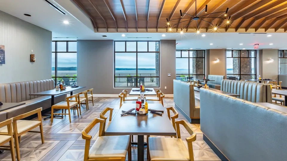 The interior of a restaurant with booths, tables and chairs looking out over a lake view