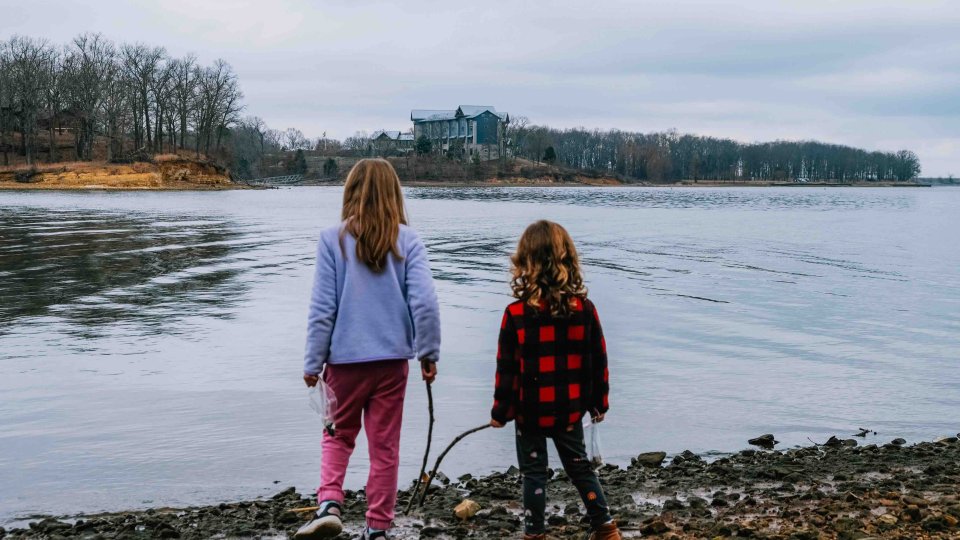 Two children holding hands by a lake with cloudy skies.