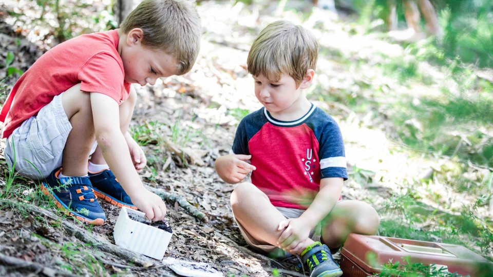 Two young boys exploring nature, playing with dirt and leaves.