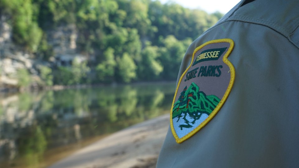 Park ranger's shoulder patch with a tranquil river landscape in the background.