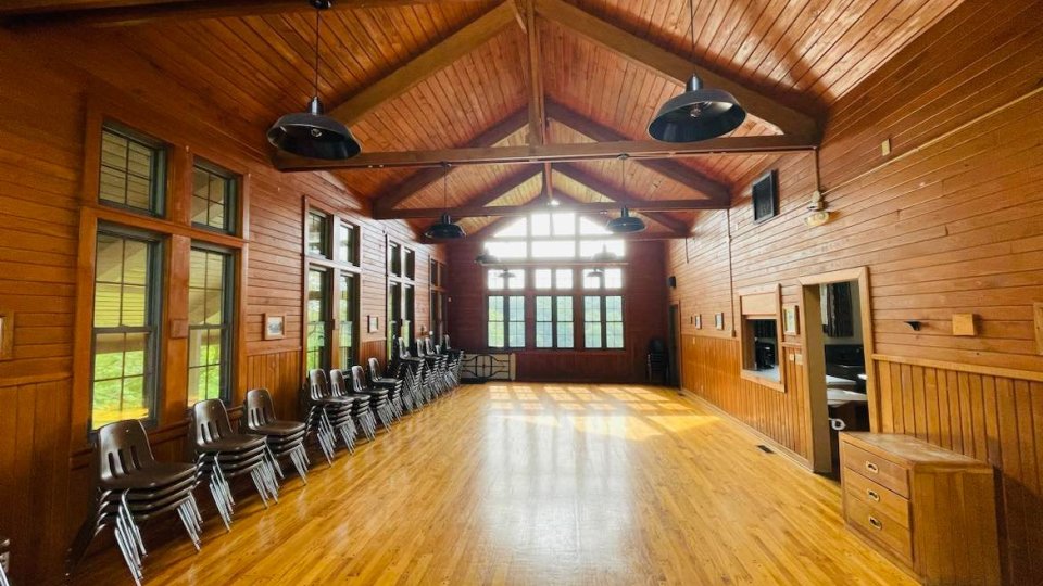 Spacious wooden hall with stacked chairs and large windows.