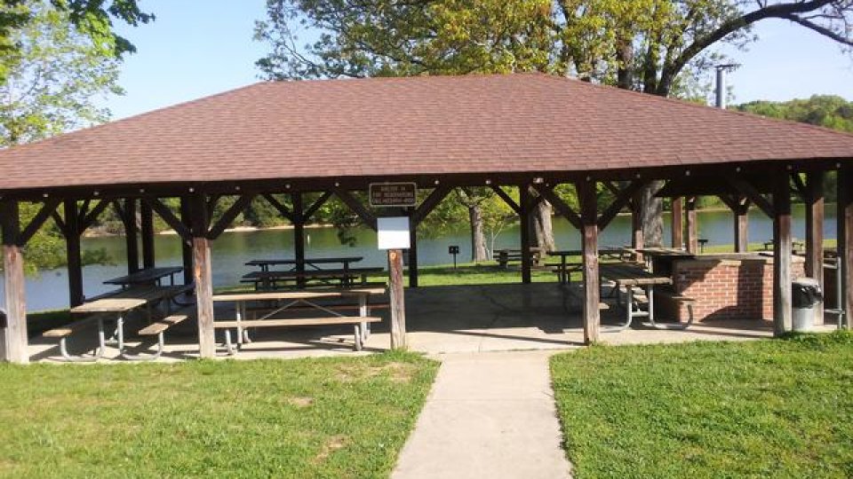 Pavilion with picnic tables by a lake on a sunny day.