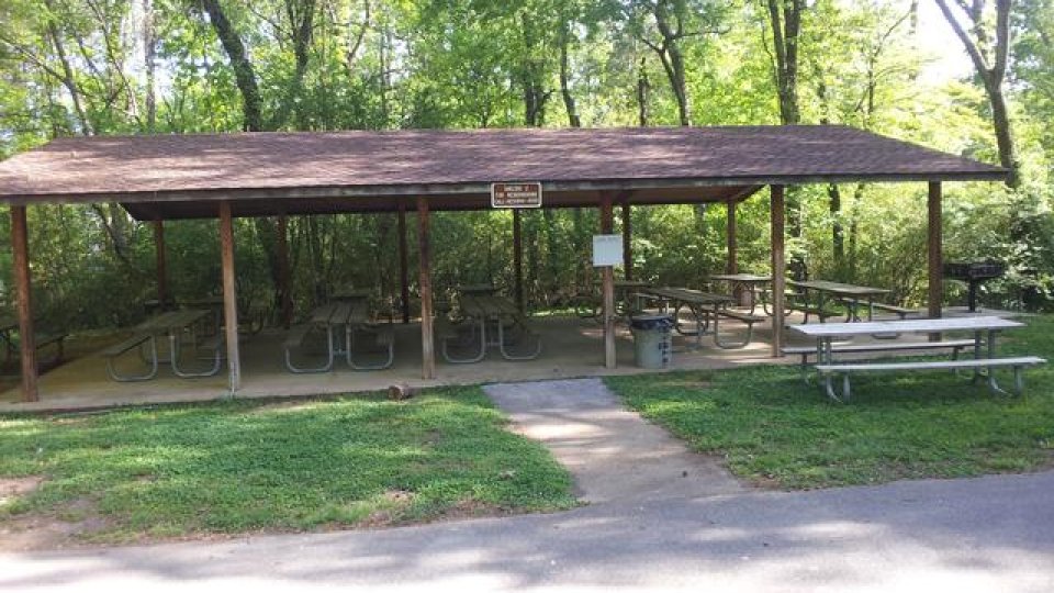 Shelter with picnic tables surrounded by trees in a park.