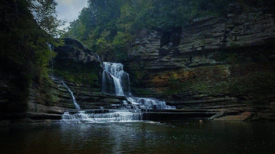 Waterfall cascading over rocky ledges into a serene forest pool.