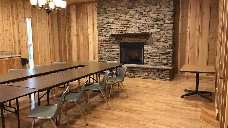 Wood-paneled meeting room with tables, chairs, and a stone fireplace.