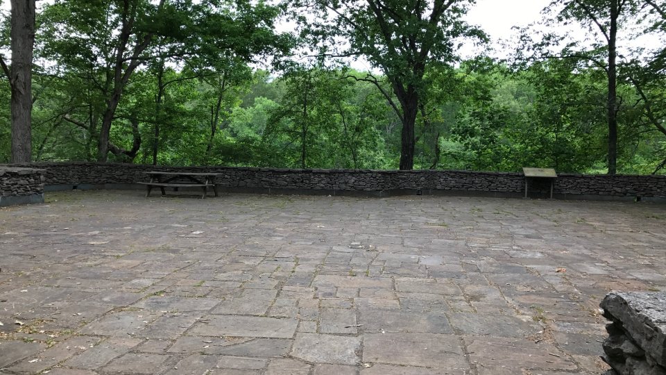 Stone patio surrounded by trees and a stone wall.