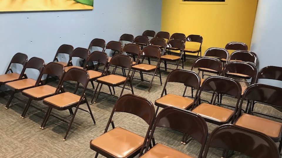 Empty room with rows of brown folding chairs and a yellow accent wall.
