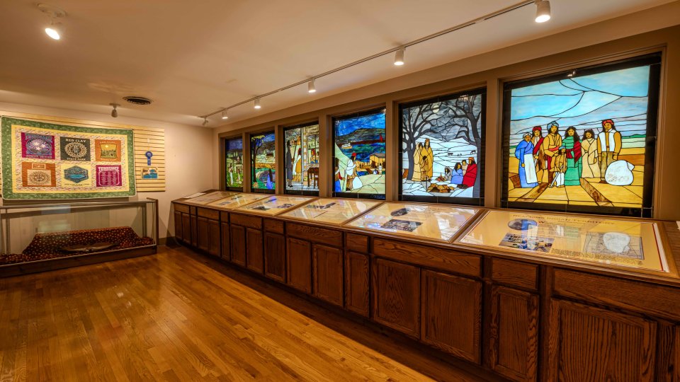 Art gallery interior with stained glass windows and display cases.