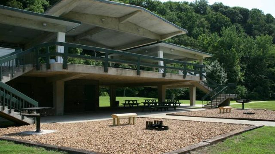 Concrete pavilion in a park with picnic tables and trees in the background.