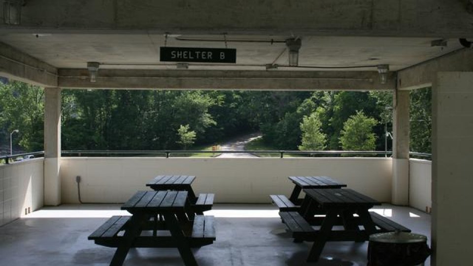 Covered shelter with picnic tables, overlooking a tree-lined path.