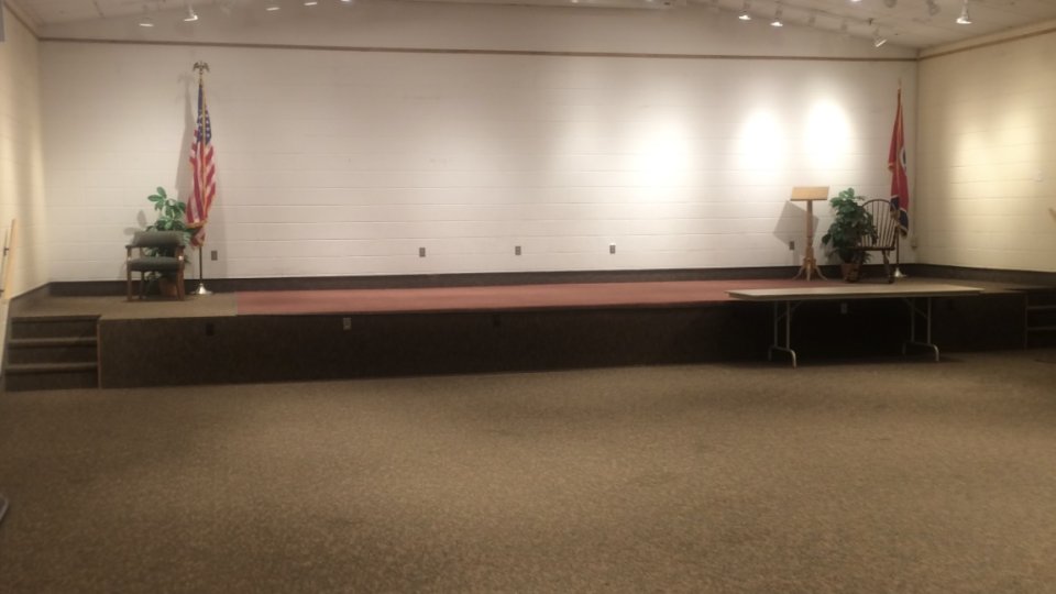 Empty auditorium with stage, flags, and bright lighting.