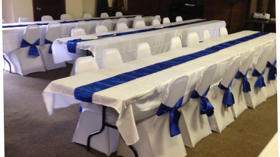 Tables with white cloths and blue bows set up in a hall.