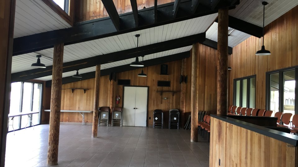 Wood-paneled room with high ceilings, large windows, and empty seating areas.