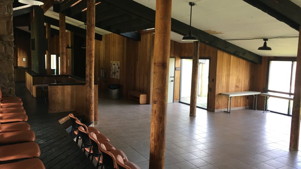 Open room with wooden beams, brown chairs, and large windows.