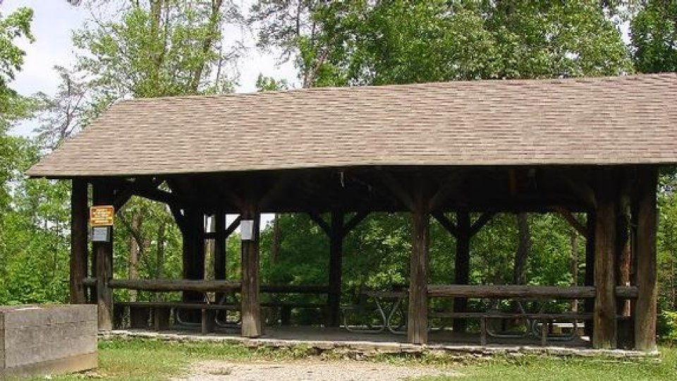Wooden pavilion in a park with a shingled roof and surrounding greenery.