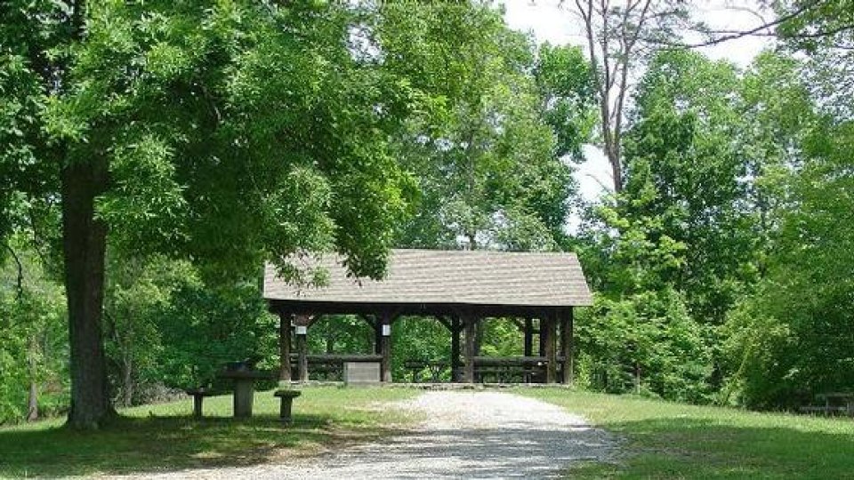 Wooden shelter in a lush park with a gravel path.